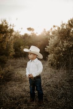 a young boy wearing a cowboy hat standing in a field