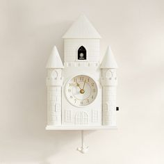 a white clock mounted to the side of a wall with a castle design on it