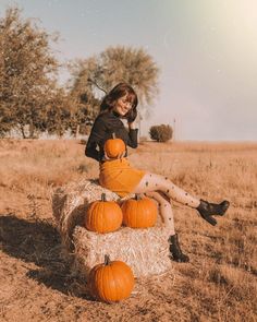 a woman sitting on top of hay bales with pumpkins