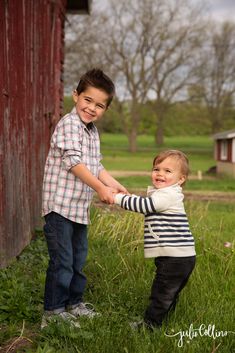 two young boys are holding hands in front of a red barn and green grass field