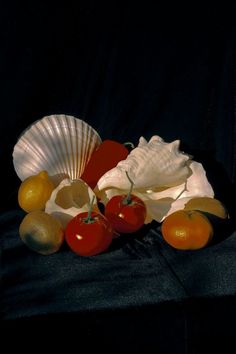 fruit and shells are arranged on a black cloth with a fan in the background,