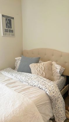 a bed with white sheets and pillows in a bedroom next to a wall mounted poster