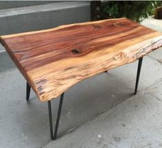 a wooden table sitting on top of a cement floor next to a potted plant