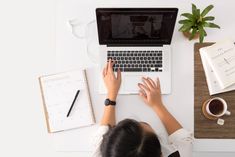 a woman sitting at a desk working on a laptop computer with her hands resting on the keyboard