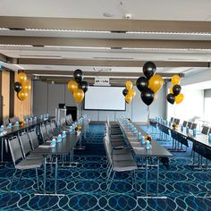 an empty conference room set up for a meeting with black and gold balloons hanging from the ceiling