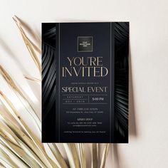 an elegant black and gold party card with palm leaves on the table next to it