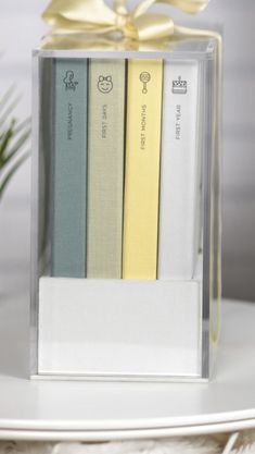 three books are in a clear box with a bow on the top one is yellow, white and blue