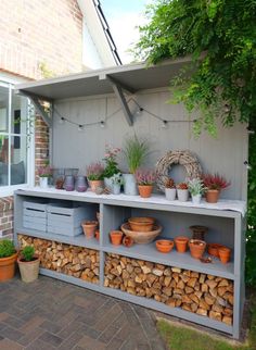 an outdoor area with potted plants and wood stacked on top of each other in front of a building