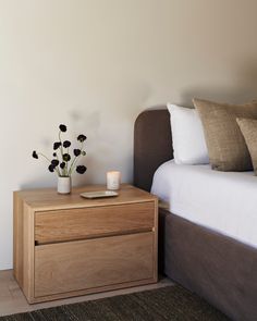 a nightstand with flowers on it next to a bed