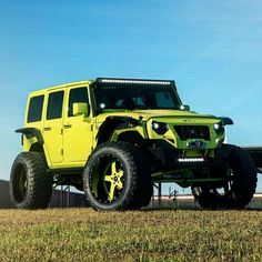 a bright yellow jeep parked on top of a grass covered field