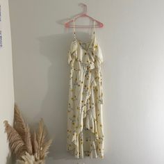 a white dress hanging on a wall next to a potted plant and dried grass