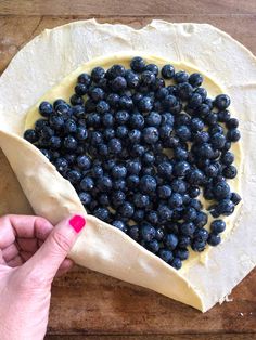 a person is placing blueberries on top of the dough in a heart shape to make a pizza