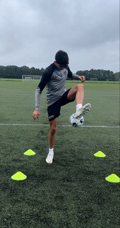 a young man kicking a soccer ball on top of a field with yellow cones in front of him