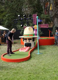 a man is playing miniature golf on the grass with other people watching him play in the background