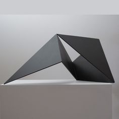 a black sculpture sitting on top of a white table next to a gray and white wall