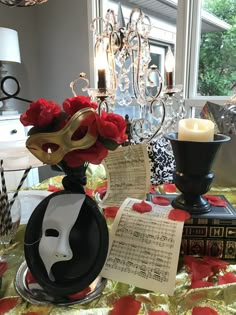 a table topped with a vase filled with red roses and sheets of paper next to a candle