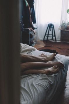 a person laying on top of a bed in a room with a wooden floor and white walls