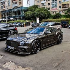 a black car parked on the side of a road next to other cars in front of tall buildings