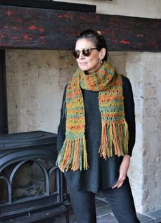 a woman standing in front of a fireplace wearing sunglasses and a scarf with tassels