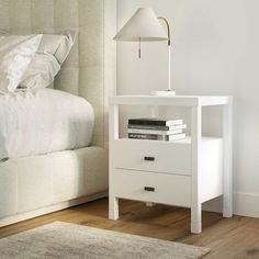 a white night stand with two drawers and a lamp next to it on a wooden floor