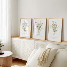 three framed flowers sit on the wall above a bed with white linens and pillows