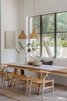 a dining room table with chairs and a bowl on top of it, in front of a large window