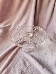 a clear glass dish on a pink cloth covered tablecloth with an object in the center