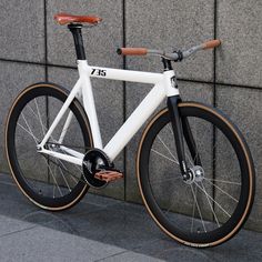 a white and brown bike parked next to a wall on the side of a street