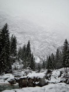 snow covered mountains and trees are in the foreground, with a stream running through it