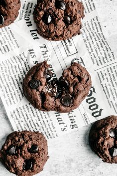 four chocolate cookies sitting on top of a newspaper