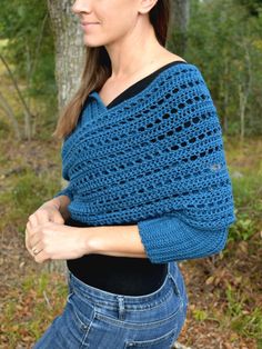 a woman is wearing a blue crocheted shawl in the woods with her hands on her hips