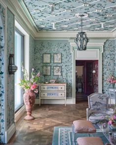 a living room filled with furniture and flowers on the wall next to a doorway that leads to another room