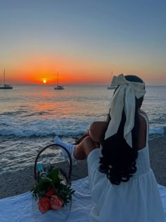 a woman sitting on the beach at sunset with her back to the camera, looking out over the water