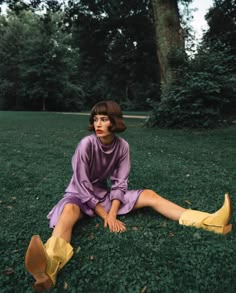 a woman sitting in the grass with her legs crossed, wearing yellow boots and a purple dress