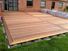 a large wooden deck in front of a brick building with grass and bushes around it