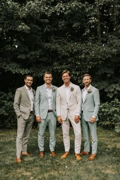 a group of men standing next to each other in front of some trees and grass