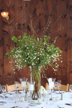 a vase with flowers and greenery is on a table set for an elegant dinner