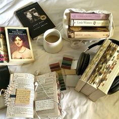 several books and headphones on a bed next to a cup of coffee, notebooks, and other items