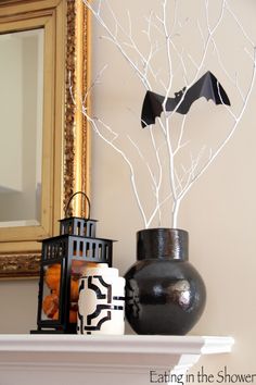 a black vase with bats on it next to a white tree branch and a mirror