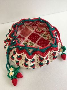 a crocheted strawberries bag sitting on top of a white table next to a red strawberry