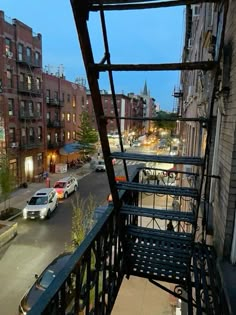 the view from an apartment balcony looking down at cars parked on the street and buildings