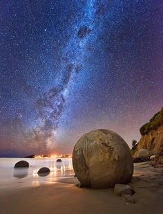 the night sky is filled with stars above some rocks on the beach and water in front of it