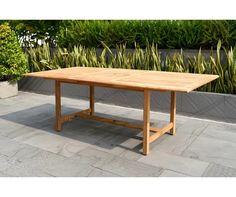 a wooden table sitting on top of a stone floor next to some plants and bushes