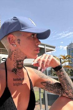 a woman with tattoos on her neck and chest sitting in front of a building wearing a baseball cap