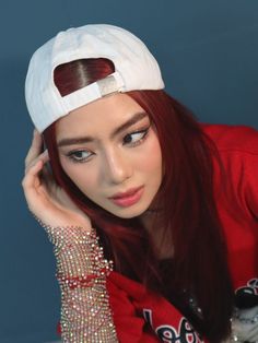 a woman with long red hair wearing a white baseball cap and beaded bracelets