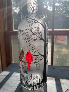 a painted glass bottle sitting on top of a table next to a window with trees