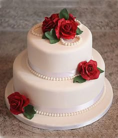 a three tiered wedding cake with red roses on the top and pearls around the edges