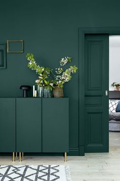 a living room with green walls and plants on the sideboard next to an open door