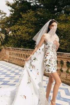 a woman in a wedding dress and veil standing on a tiled floor with trees behind her