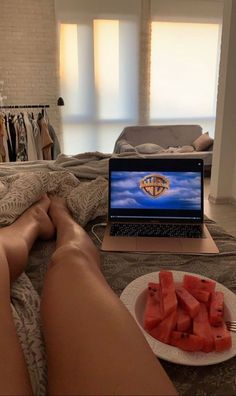 a person laying on a bed with their legs crossed next to a plate of watermelon slices